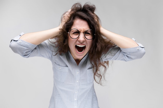 Young brunette girl with glasses. The girl grabbed her head and shouted.