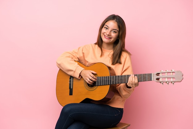 Giovane ragazza castana con la chitarra sopra il rosa isolato