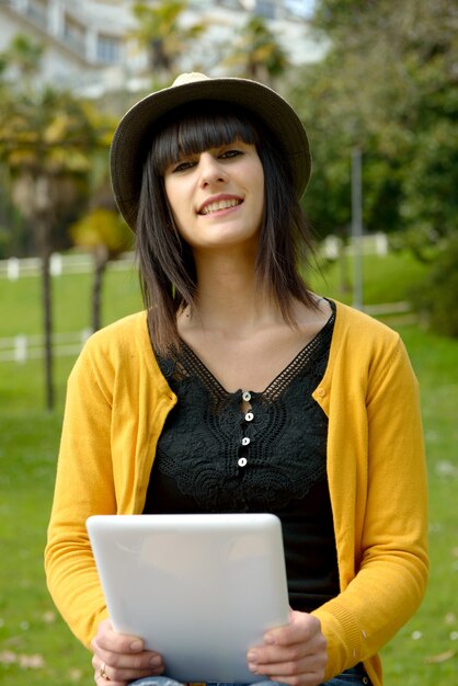 外の公園でタブレットで若いブルネットの少女