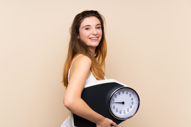 Young brunette girl  with weighing machine over isolated wall