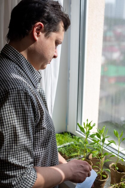 ソーサーで自宅のエコポットで苗に水をまく宿題をしている若いブルネットの男家の園芸植物の世話