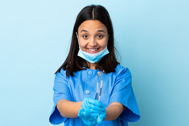 広告を挿入する手のひらに架空のcopyspaceを保持している孤立した背景にツールを保持している若いブルネットの混合レース歯科医女性