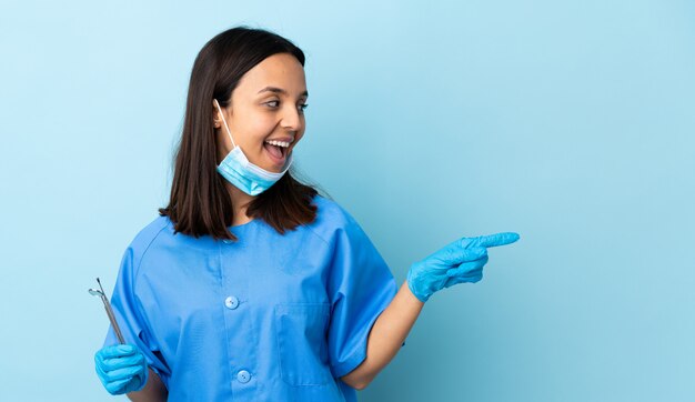 若いブルネットの混合レース歯科医の女性が指を持ち上げながら解決策を実現しようとする孤立した背景の上にツールを保持