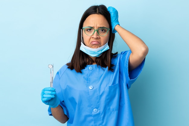 Young brunette mixed race dentist woman holding tools over isolated with an expression of frustration and not understanding