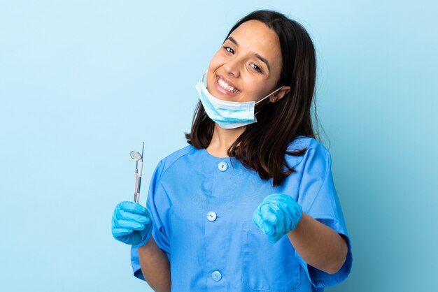 Young brunette mixed race dentist woman holding tools pointing front with happy expression