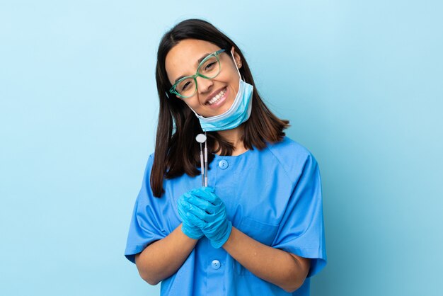 Young brunette mixed race dentist woman holding tools over wall keeps palm together