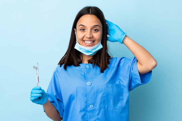 Молодая брюнетка смешанной расы стоматолог женщина держит инструменты над стеной смеется