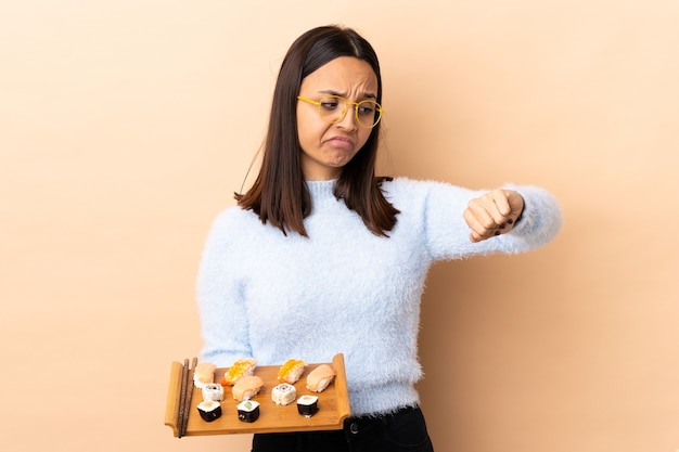 Young brunette mixed race woman holding sushi over isolated background making the gesture of being late