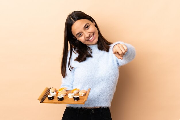 Young brunette mixed race woman holding sushi over isolated  pointing front with happy expression