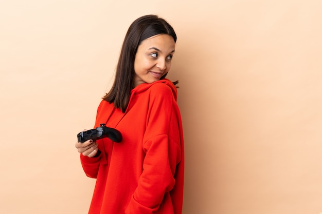 Young brunette mixed race woman playing with a video game controller over isolated laughing