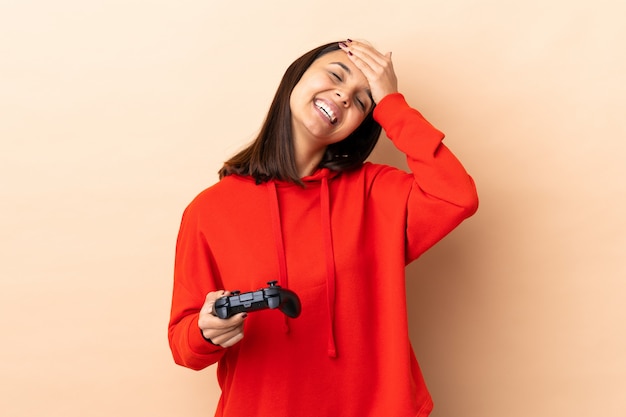 Young brunette mixed race woman playing with a video game controller over wall laughing