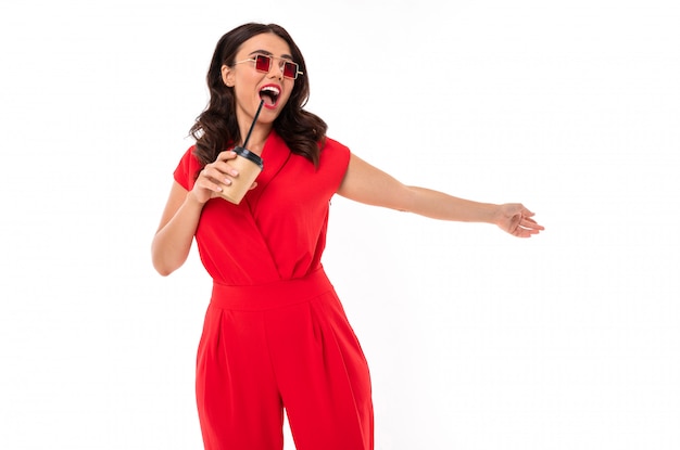 Young brunette in a red dress with a glass of coffee in her hands, a girl in sunglasses with a smile