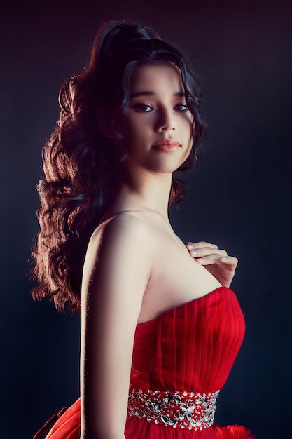 Young brunette in a red puff dress on dark background