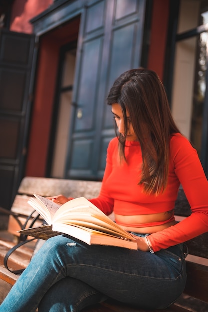 Young brunette sitting on a bench in the park reading a book