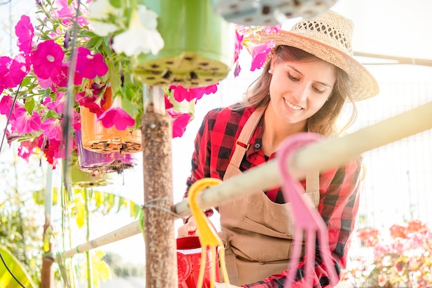 Foto la giovane donna sorridente del brunette tratta gentilmente i fiori in una serra. immagine colorata e vibrante