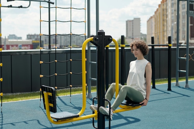 Молодая брюнетка-спортсменка в спортивной одежде сидит на спортивных сооружениях