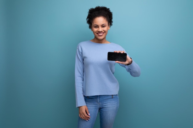 Young brunette swarthy skin woman holding smartphone horizontally with mockup for web page