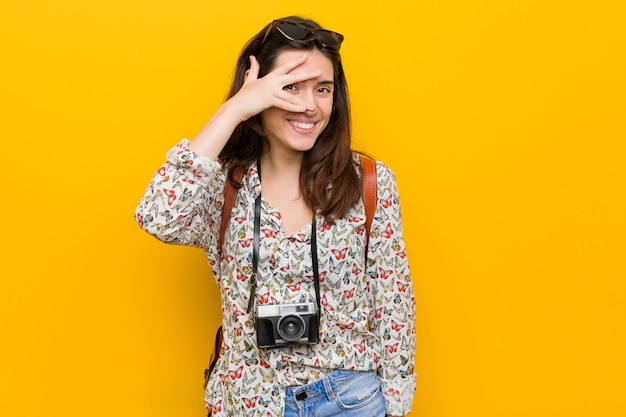 Young brunette traveler woman blink at through fingers, embarrassed covering face.