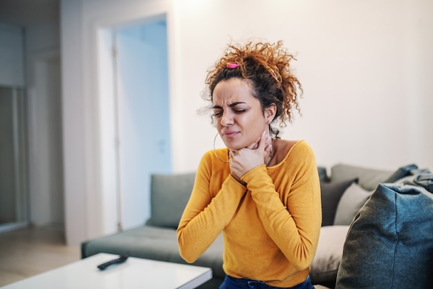 Photo young brunette with curly hair pain in throat.