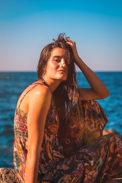 Молодая брюнетка с мокрыми волосами и цветочным платьем у моря, летний стиль жизни