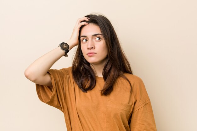 Young brunette woman against a beige being shocked, she has remembered important meeting.