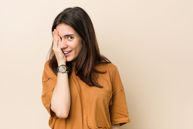 Young brunette woman against a beige  having fun covering half of face with palm.