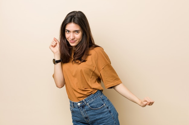 Young brunette woman against a beige wall dancing and having fun.