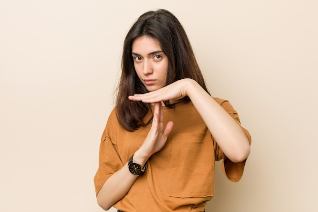 Young brunette woman against a beige wall showing a timeout gesture.