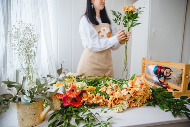 A young brunette woman in an apron in the process of creating a bouquet in the rustic style in her flower shop