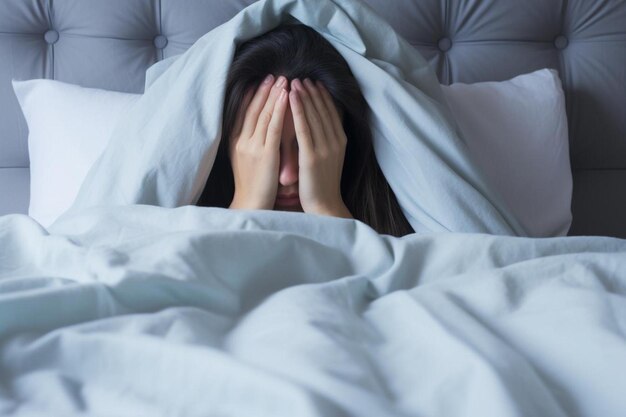 young brunette woman in bed covering face with hands concept of exhaustion grief sadness loneliness