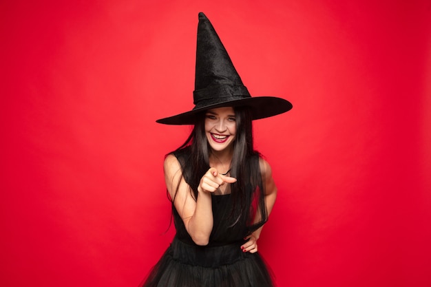 Young brunette woman in black hat and costume on red background Attractive