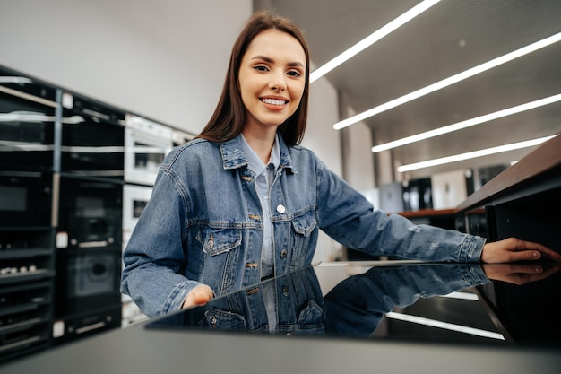 Young brunette woman choosing new electric stove in a hypermarket