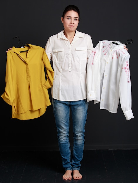 Young brunette woman choosing one shirt of two