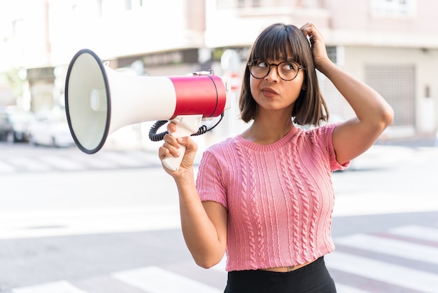 Photo young brunette woman in the city holding a megaphone and having doubts