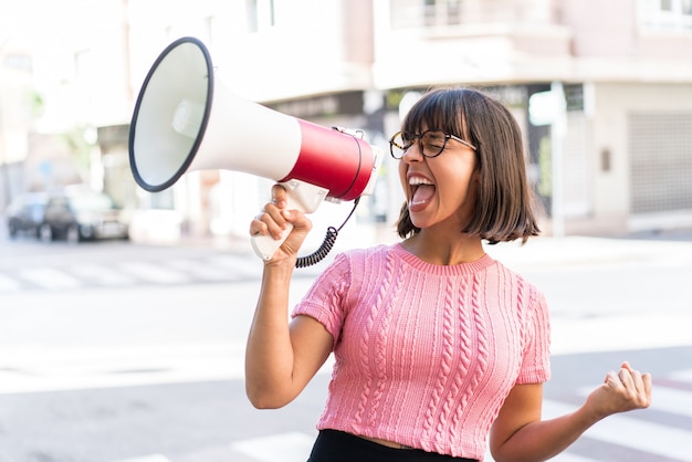 Young brunette woman in the city shouting through a megaphone to announce something in lateral position