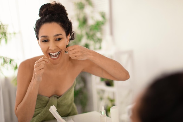 Young brunette woman cleaning teeth with dental floss near\
mirror at home copy space oral hygiene