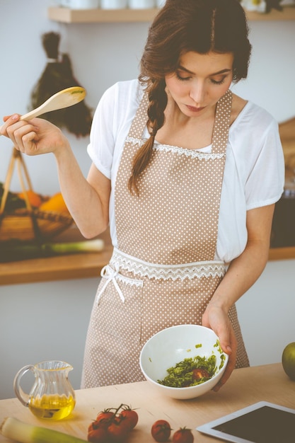 Young brunette woman cooking in kitchen. Housewife holding wooden spoon in her hand. Food and health concept.