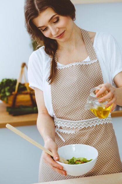 부엌에서 요리하는 젊은 갈색 머리 여자. 그녀의 손에 나무로 되는 숟가락을 들고 주부입니다. 음식과 건강 개념입니다.