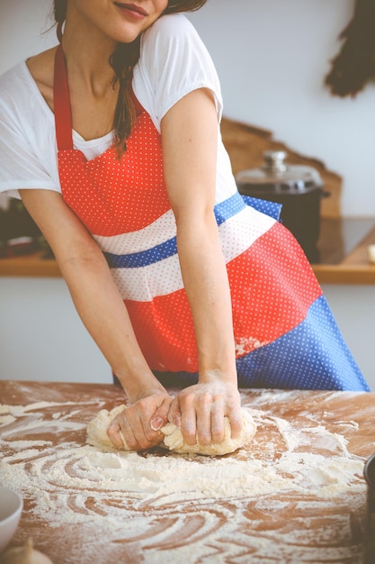 Молодая брюнетка готовит пиццу или макароны ручной работы на кухне. Домохозяйка готовит тесто на деревянном столе. Концепция диеты, еды и здоровья.