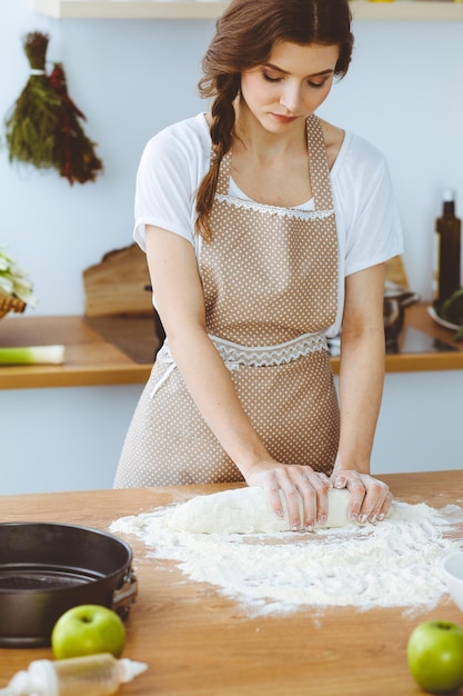 부엌에서 피자나 수제 파스타를 요리하는 젊은 브루네트 여성. 나무 테이블에 반죽을 준비 하는 주부. 다이어트, 음식 및 건강 개념입니다.