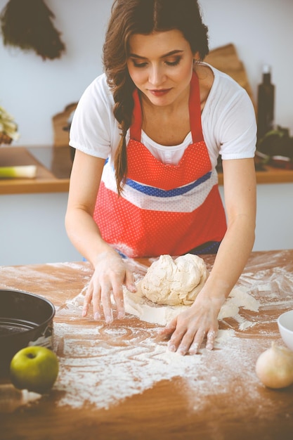 Фото Молодая брюнетка готовит пиццу или макароны на кухне. домохозяйка готовит тесто на деревянном столе. диета, еда и концепция здоровья.