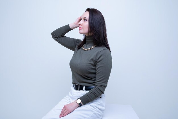 A young brunette woman in a dark golf and light jeans poses in\
the studio