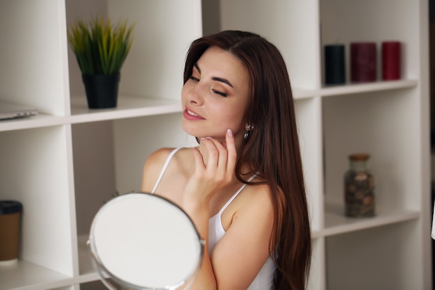 Young brunette woman doing her skincare in the mirror