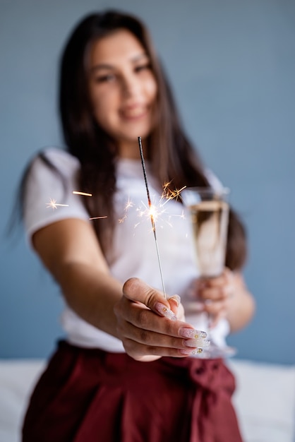 線香花火を保持しているシャンパンを飲む若いブルネットの女性