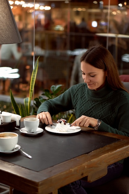 Young brunette woman drinking coffee in a cafe and eating dessert