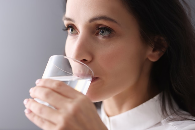 Young brunette woman drinking water from glass. Sufficient fluid intake concept