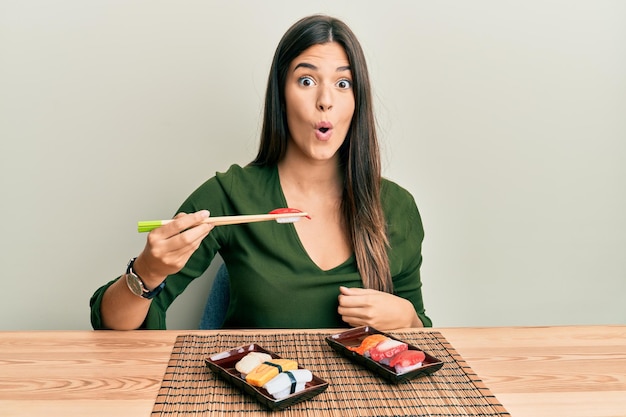 Photo young brunette woman eating sushi sitting on the table scared and amazed with open mouth for surprise disbelief face