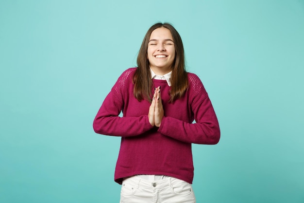 Young brunette woman girl in casual clothes posing isolated on blue green turquoise background studio portrait. People sincere emotions lifestyle concept. Mock up copy space. hands folded in prayer.