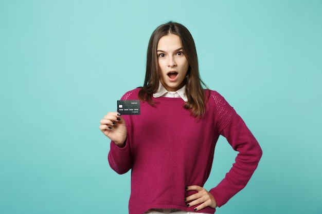 Young brunette woman girl in casual clothes posing isolated on blue turquoise background studio portrait. People sincere emotions lifestyle concept. Mock up copy space. Hold in hand credit bank card.