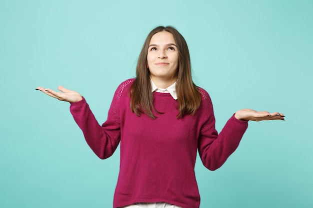 Young brunette woman girl in casual clothes posing isolated on blue turquoise wall background studio portrait. People sincere emotions lifestyle concept. Mock up copy space. Looking up spreading hands